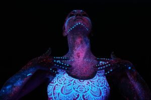 Art woman cosmos in ultraviolet light. Entire body is covered with colored droplets.