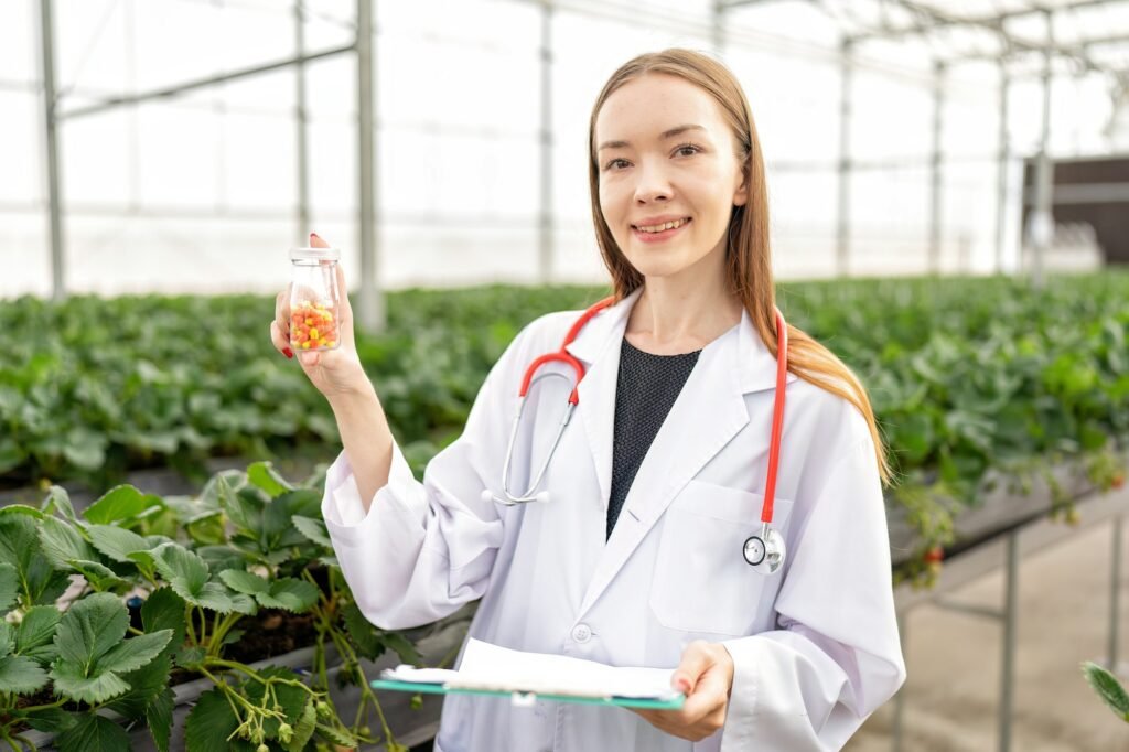 Doctor nutritionist in greenhouse farming proudly showing bottle of fruit vegetable extract pill