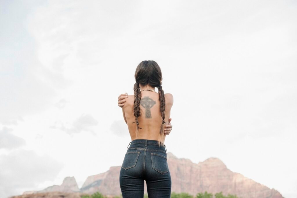 Rear view of Topless young woman wearing jeans, tattoo of a Celtic Cross