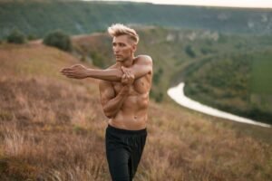 Sportive shirtless man stretching muscles on nature
