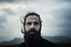 A man with black hair, a full beard and moustache.