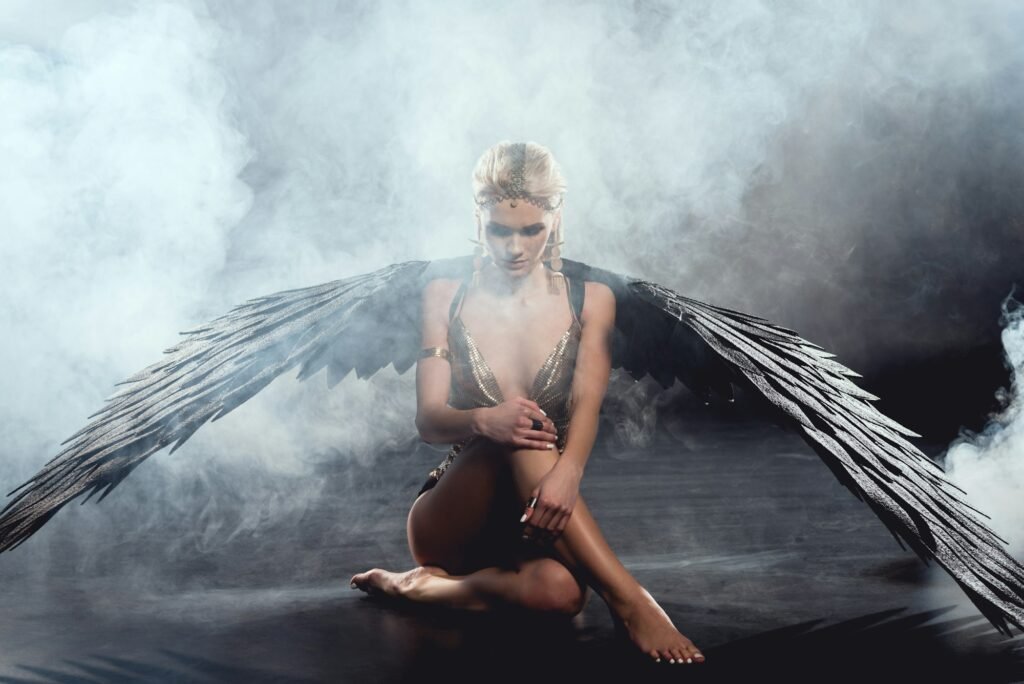 beautiful sexy woman with black angel wings sitting and posing on dark background