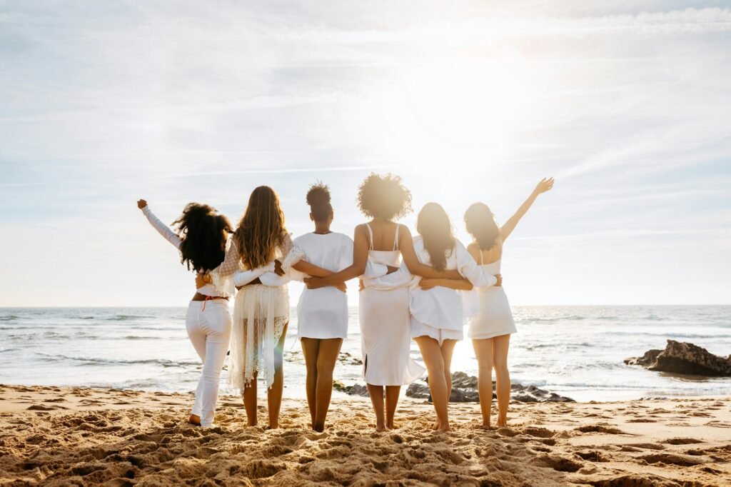 Bride's team. Back view of group of young diverse women posing and embracing by the seashore. Hen