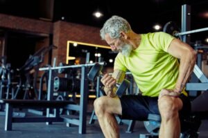 Gaining muscles after 40. Strong mature man in sportswear lifting heavy dumbbells and pumping his