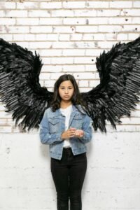 Girl standing in a wall with black wings