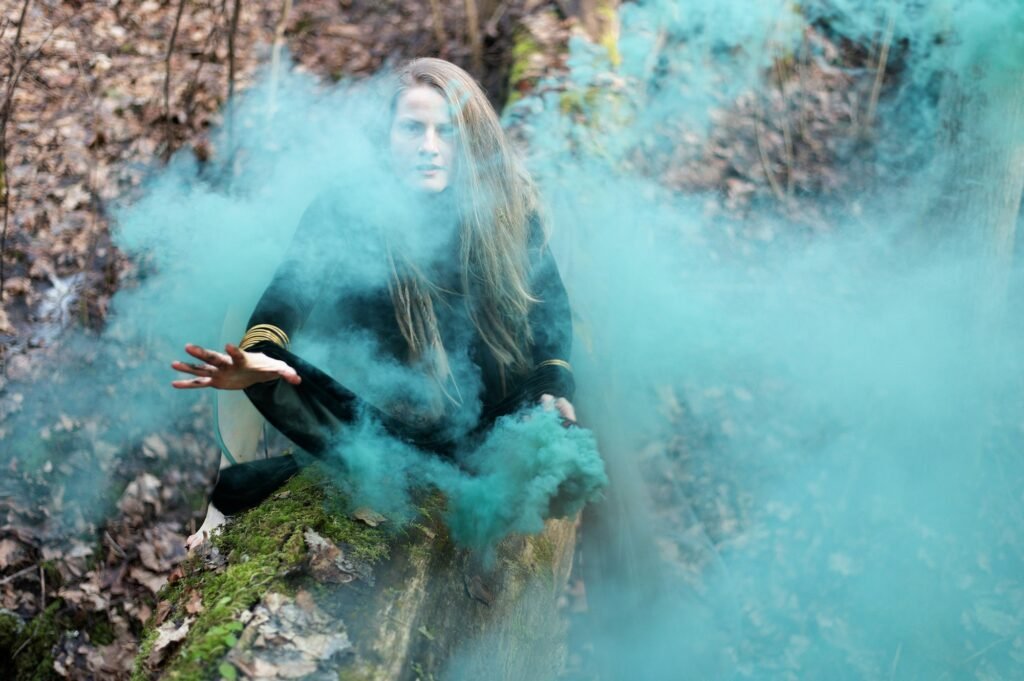Shaman female holding hand green smoke bomb on tree trunk in sping day